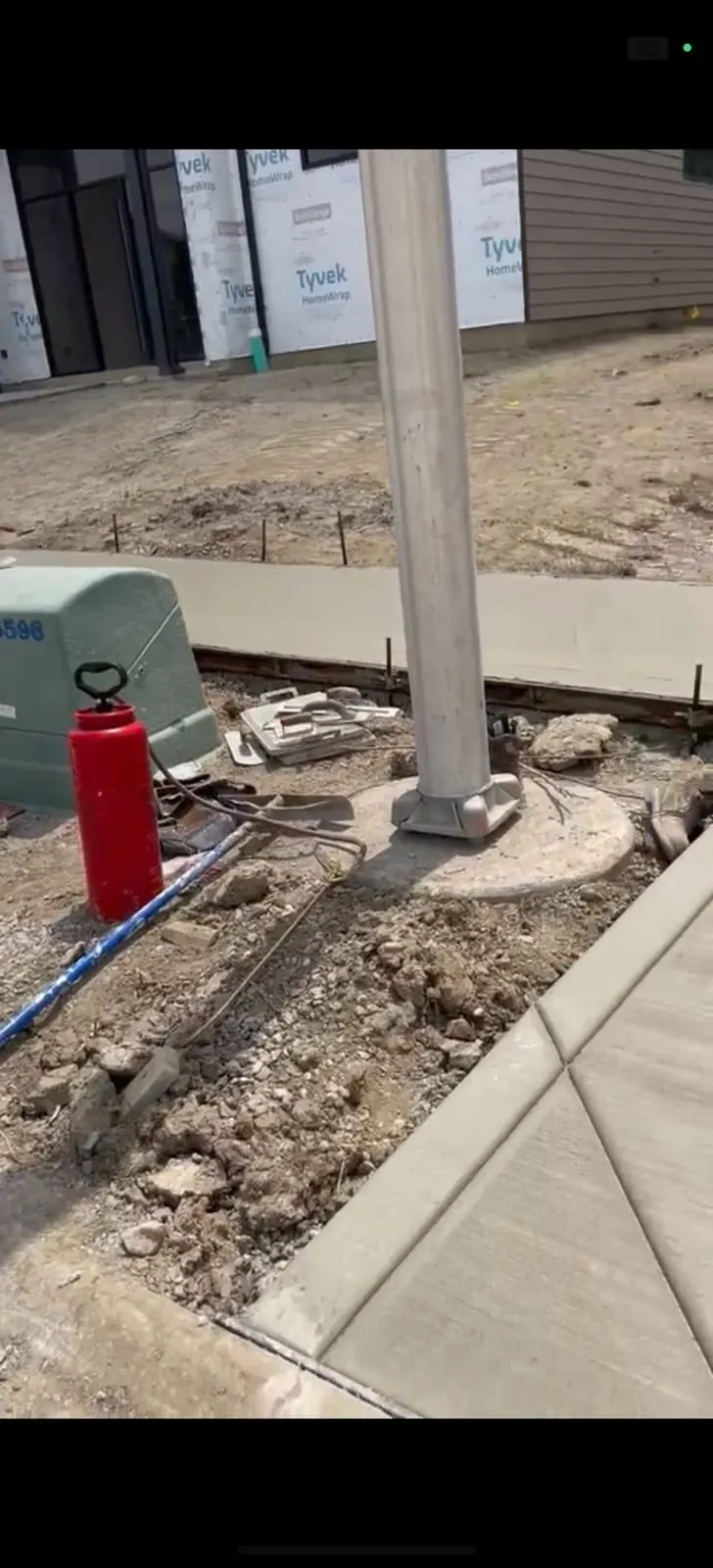 Concrete walkway poured around a light pole base near new home construction
