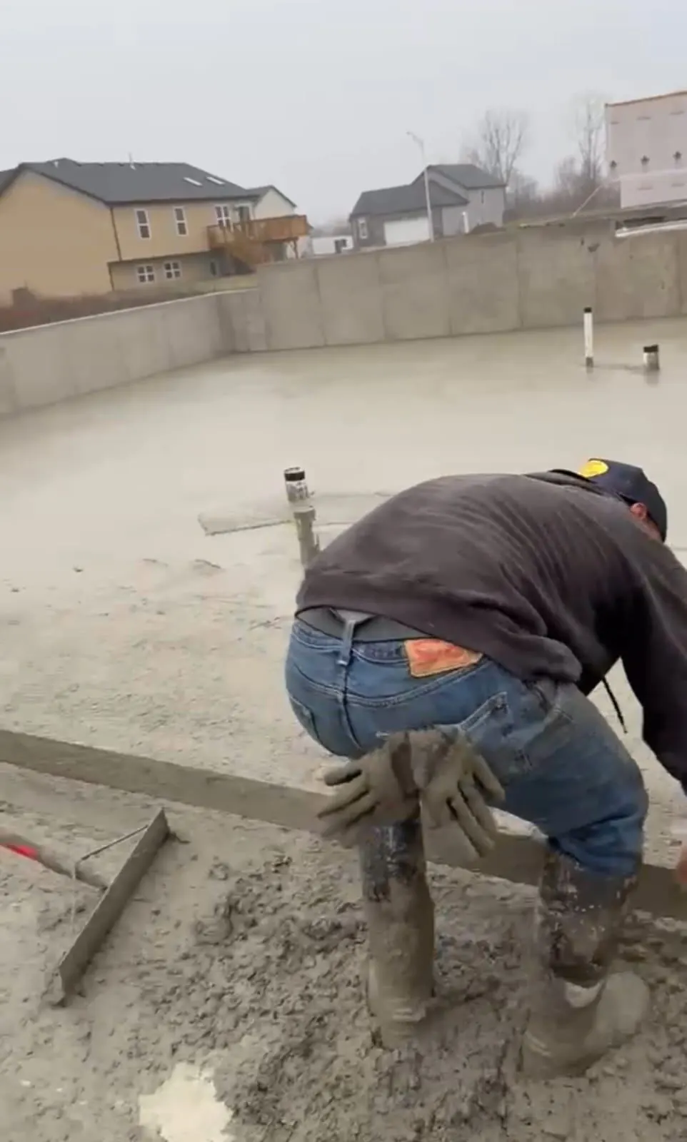 Crew hand-finishing a large basement slab pour with a bull float inside foundation walls