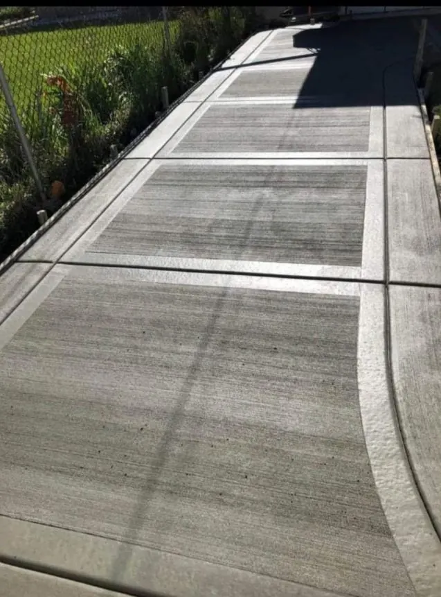 Broom-finished concrete walkway with scored panel joints along a fence line