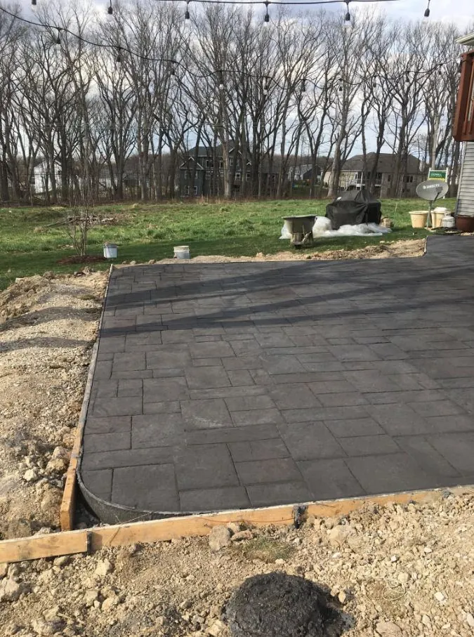 Dark charcoal stamped concrete patio with a square-tile pattern, freshly poured with wood edge forms
