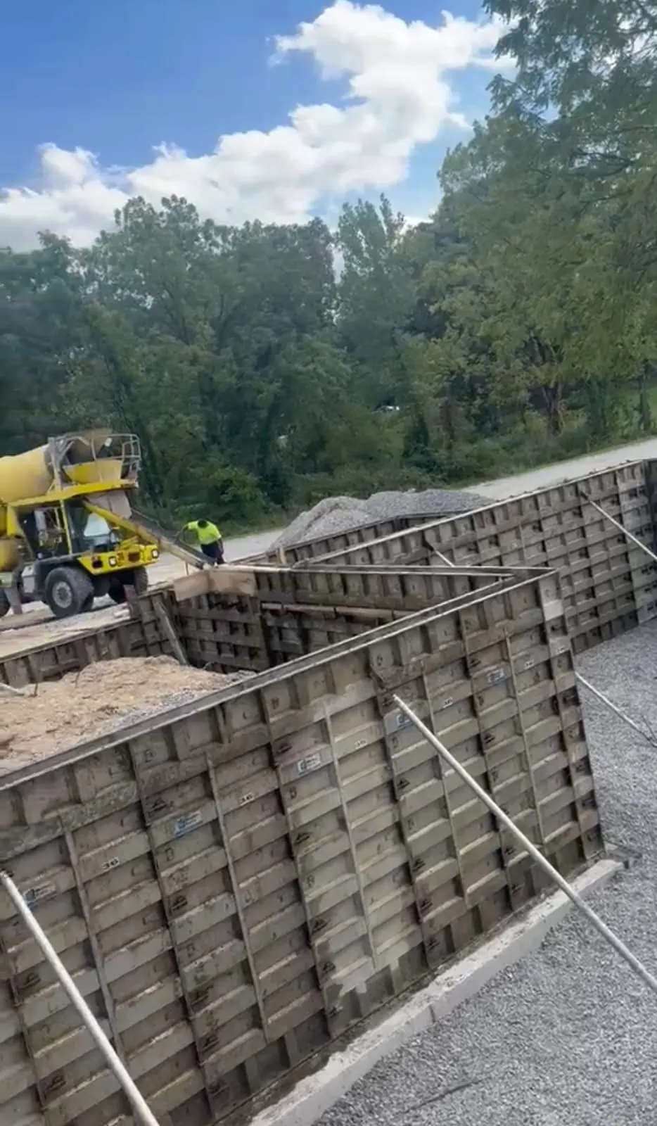 Concrete mixer truck pouring footings into wall forms over a gravel base