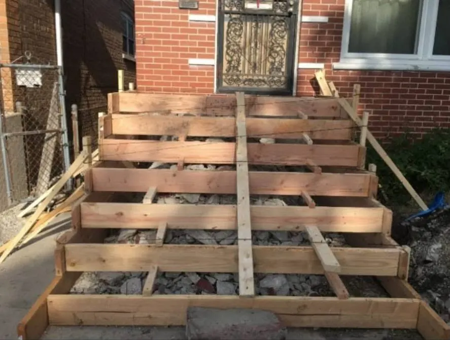Wood formwork for concrete steps in front of a brick house with a wrought iron security door