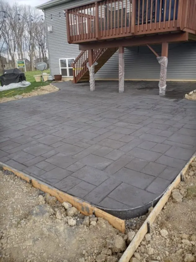 Dark stamped concrete patio in an ashlar pattern beneath a raised wood deck