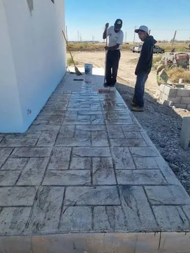 Crew finishing a stamped concrete walkway along a building exterior