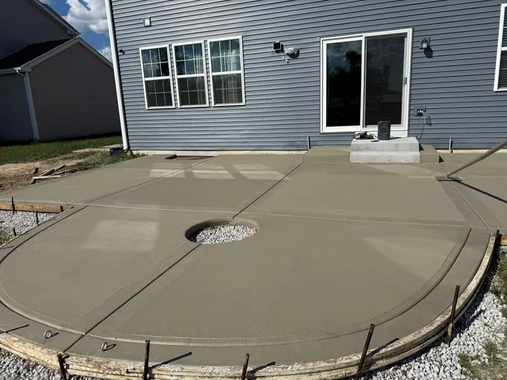 Broom-finished concrete patio with a circular gravel fire pit cutout, forms still in place