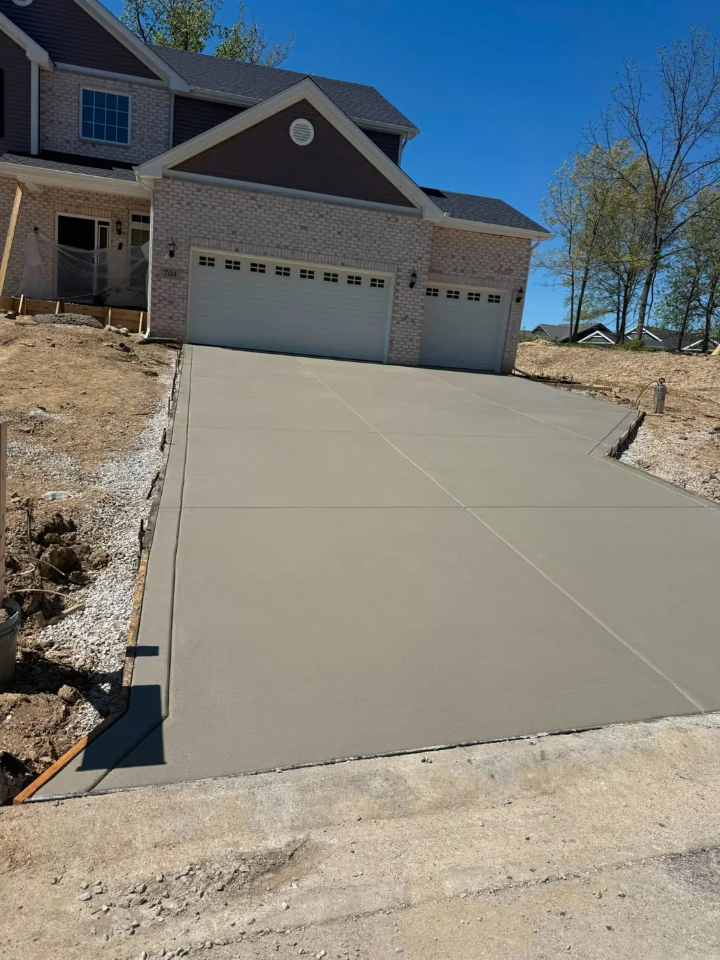 Sloped concrete driveway poured for a brick two-story home with gravel edging