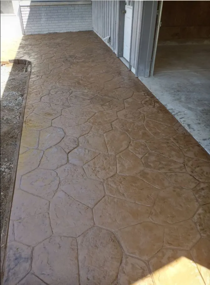 Stamped concrete walkway in a flagstone pattern along the side of a house, tan finish