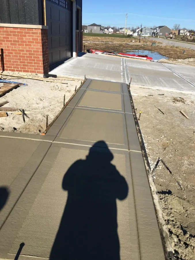 Freshly poured concrete walkway leading to a garage, broom finish curing next to a brick building