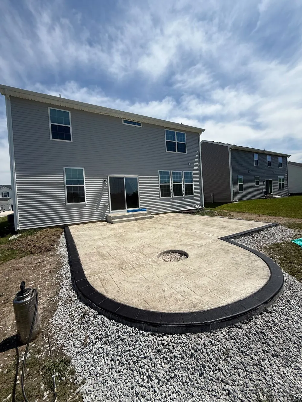 Curved stamped concrete patio with a fire pit cutout and dark charcoal border behind a two-story house